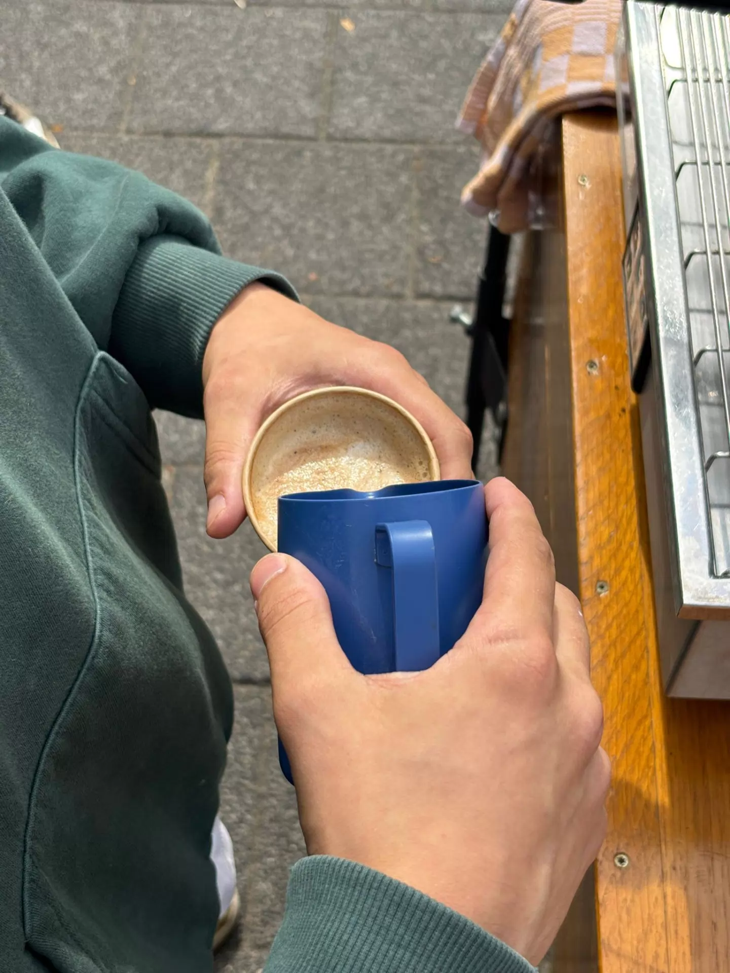 A barista pours a cappuccino from a blue milk jug at the Coffee Roamer bike